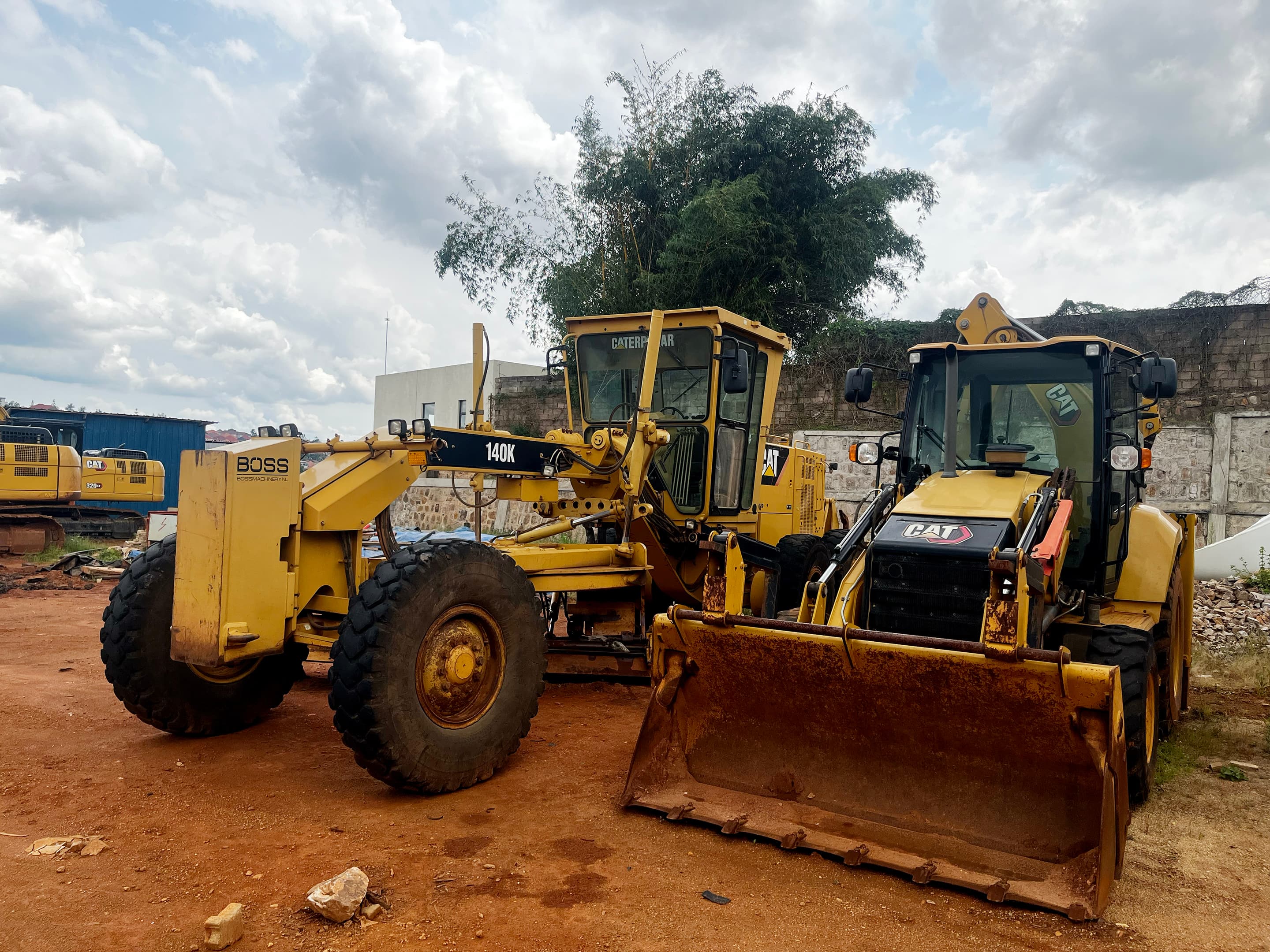 CAT backhoe loader and motor grader staged on a KAYOS yard