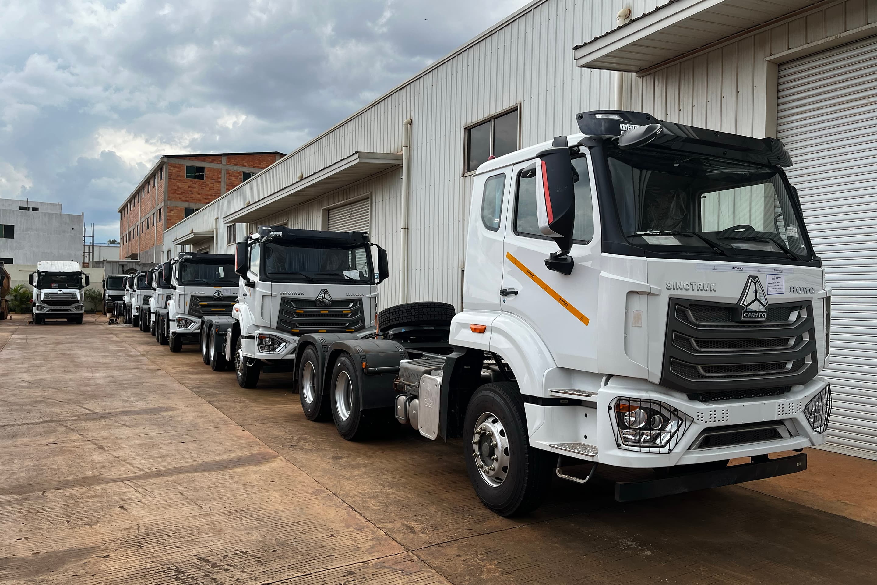 A line of KAYOS dump trucks parked at a warehouse yard